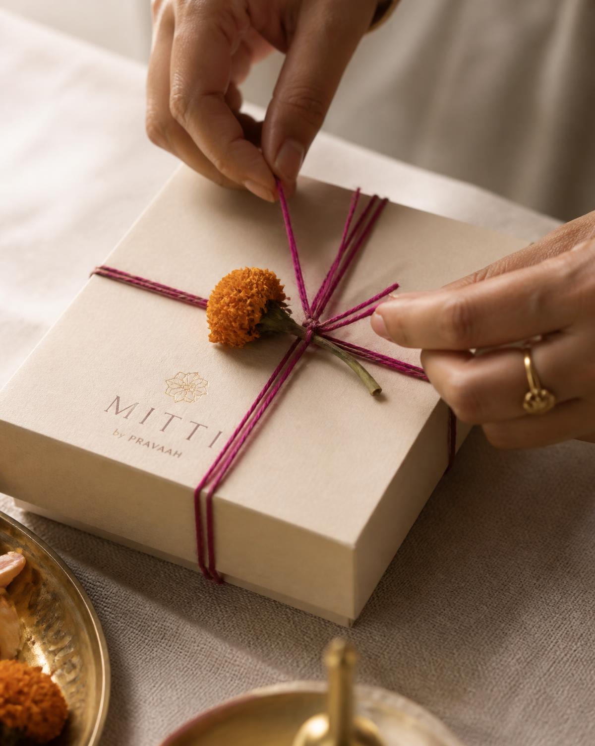 Hands tying a magenta thread and dried marigold around a kraft gift box